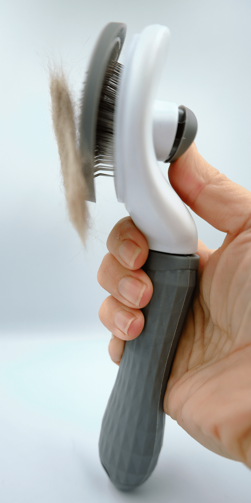 Self-cleaning cat grooming brush held in hand, showing pin bristles