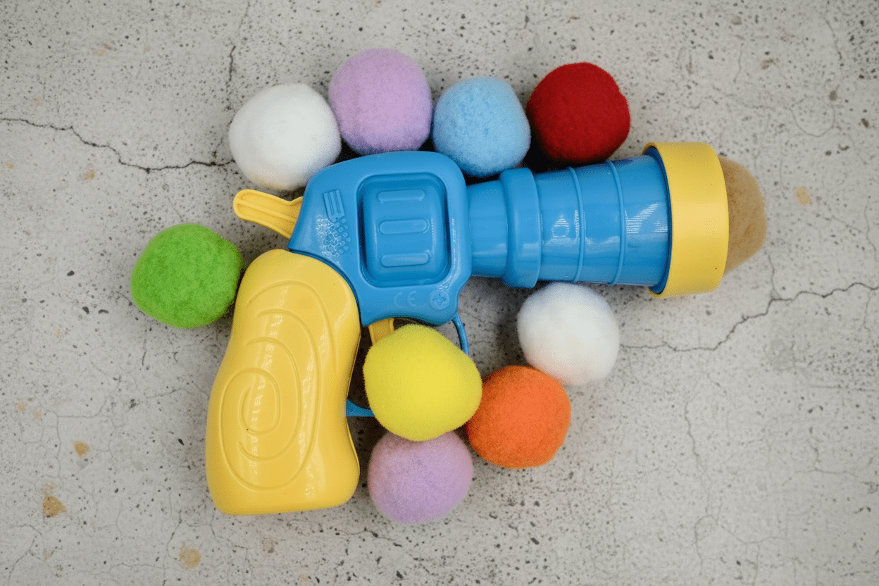 Blue and yellow cat ball launcher with multicolor plush balls surrounding the nozzle