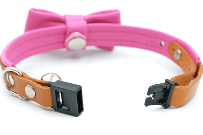 Pink leather cat collar close-up with black clasp, metal ring, and bell hardware