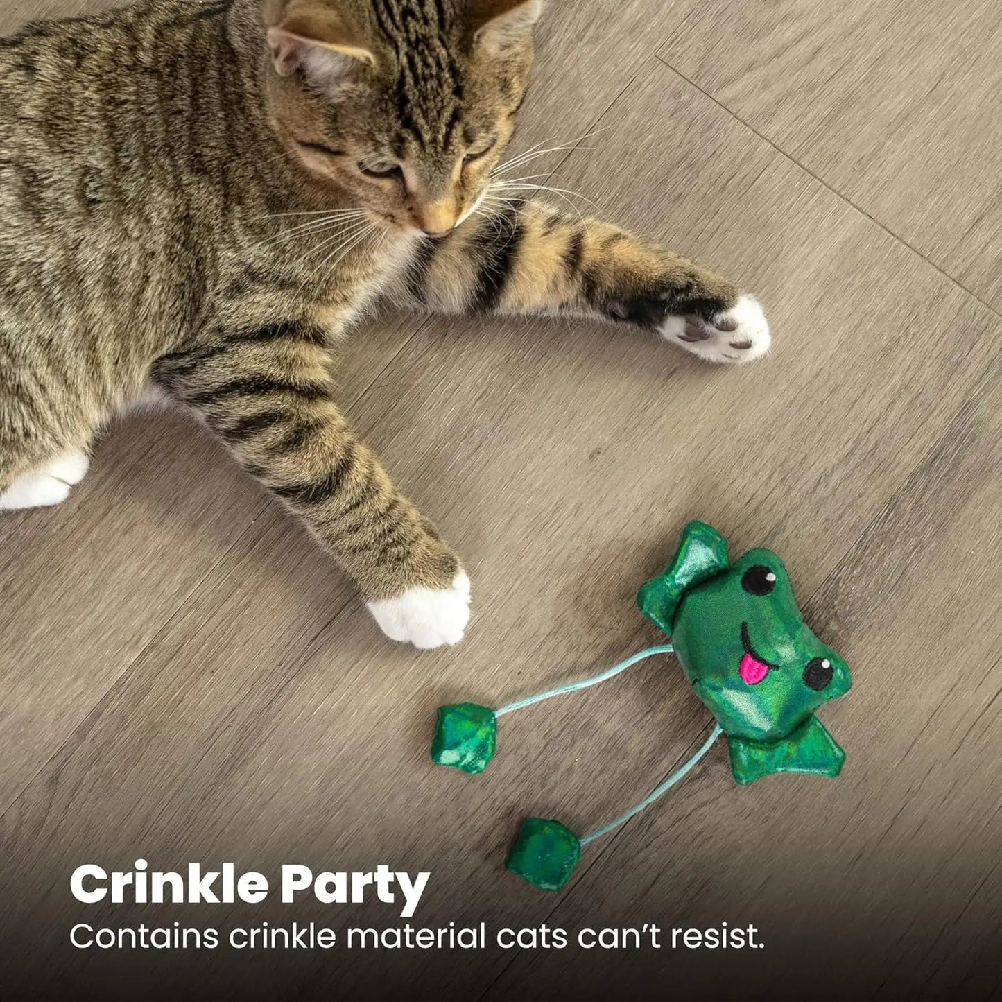 Green plush frog cat toy with dangling strings near a tabby cat, crinkle style